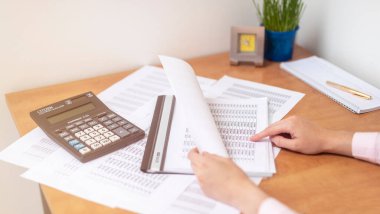 Muhasebeci ya da bankacı, masa başında dokümanlara işaret eden belgelerle ofis masasında hesaplamalar yapıyor. Tasarruf, finans ve ekonomi konsepti, belgelerle çalışmak