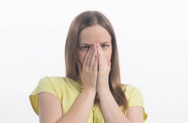 Üzgün üzgün, şaşkın, şaşkın, ağzı iki eliyle kapalı genç bir kadın. Gri arka planda izole edilmiş bir kadın, stüdyoda sarışın Avrupalı bir kadın.