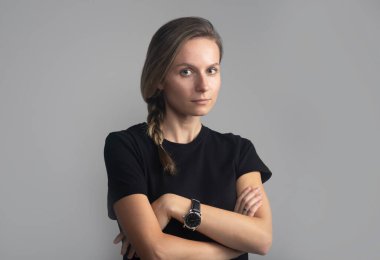 Stüdyo başı ve omuzları gri üzerinde siyah tişörtlü, kameraya bakan genç ve güzel bir kadının portresi.