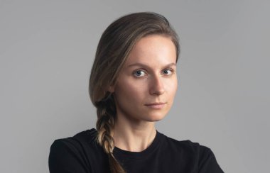 Stüdyo başı ve omuzları gri üzerinde siyah tişörtlü, kameraya bakan genç ve güzel bir kadının portresi.