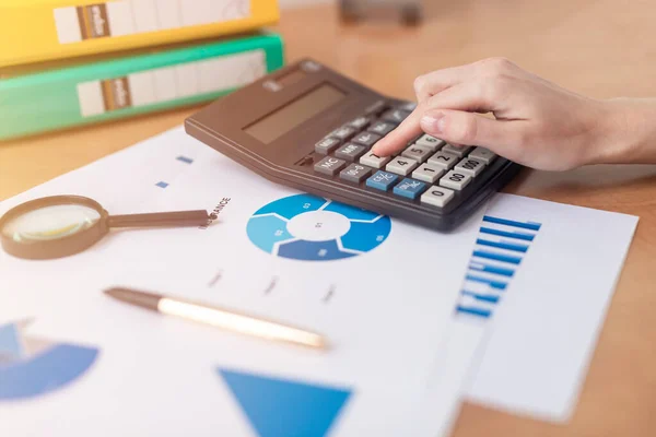 female accountant or banker making calculations sitting at office table with documents with tables on desk. Savings, finances and economy concept, counting on calculator