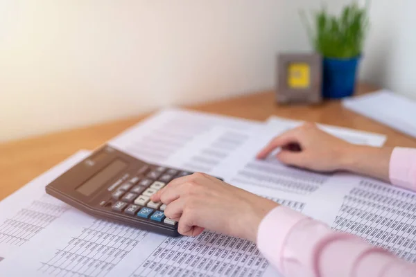 female accountant or banker making calculations sitting at office table with documents with tables on desk. Savings, finances and economy concept, counting on calculator