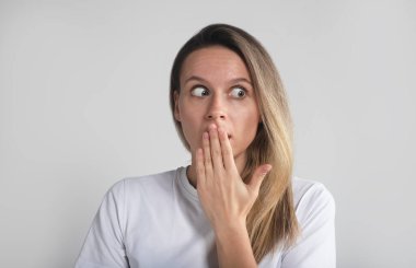 Güzel sarışın kız şokta ve ağzı kapalı, elleri gri stüdyo geçmişine bakıyor..