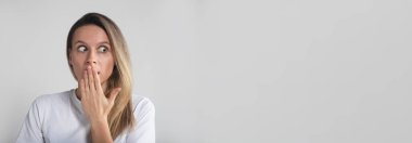 Şokta olan sarışın güzel bir kız. Gri stüdyo arka planına bakan elleri ile ağzını kapatıyor. kopyalama alanı, afiş