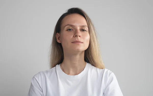 stock image caucasian woman in white t-shirt, close up, expressing arrogance and confidence, against gray background. Girl is proud of her achievements looking down to camera.