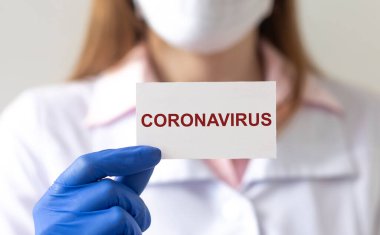 Koronavirüs kavramı. Beyaz kağıda yazılı 2019-nCoV kelime koruyucu eldivenler ve yüz maskesi içinde doktorun ellerinde.