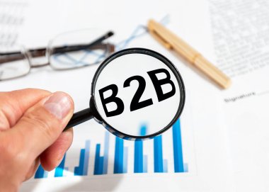 Sözcük kısaltması b2b 'den büyüteçle erkek eline mavi ve beyaz mali belgeler. İş konseptine.