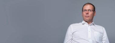 İnanılmaz bir haber. Tişörtlü, şaşırmış olgun bir adamın portresi. Gözlerini açık tutuyor ve gri arka planda otururken kameraya bakıyor. kopyalama alanı, afiş