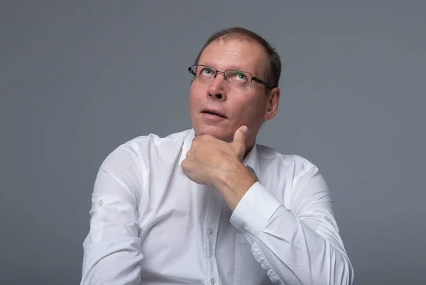 Portrait Of Thoughtful pensive serious Senior Businessman Over gray Background. spectacles and white shirt