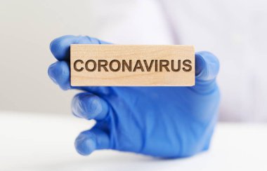 Coronavirus COVID sözcüğü ahşap blokta mavi koruyucu eldivenli doktorun elinde. beyaz arkaplan.