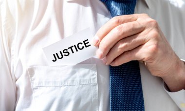 Beyaz gömleğin cebinde avukatın kravatıyla beyaz kâğıt karta yazılmış adalet sözcüğü.