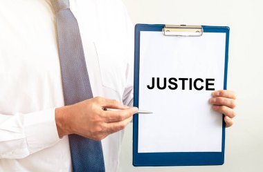 Adalet sözcüğü beyaz kağıda yazılı gömlekli ve kravatlı avukatın ellerinde.