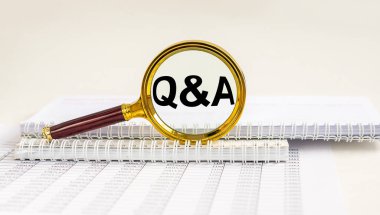 Soru ve cevaplar konsepti - Q ve A - büyüteç, ofis masasında dökümanlarla birlikte defter.