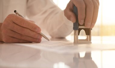 Belgeyi damgalıyor ve imzalıyor. Kapatılıyor. Erkek, parlak masasını yansıtmalı olarak teslim ediyor..