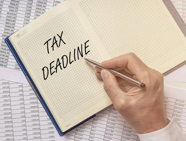 text TAX DEADLINE inscription on notebook on financial documents with male hand with pen, top view, flatly