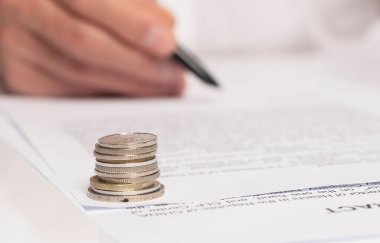 Sözleşme imzalama konsepti. İşadamı elinde kalemle belgeyi kapatıyor. para sikkeleri ön plana odaklı.