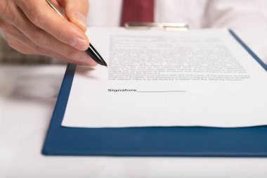 İşadamı belgelere uzanıyor ve onları imzalamayı teklif ediyor. Altın kalemle imza için yer gösteriyor..