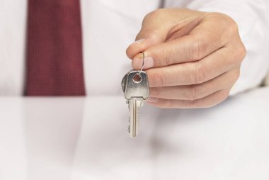 Kravatlı bir işadamının eli, beyaz masanın üzerinde duran ve yansıması olan yeni bir daireden anahtar veriyor..