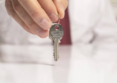 Kravatlı bir işadamının eli, beyaz masanın üzerinde duran ve yansıması olan yeni bir daireden anahtar veriyor..