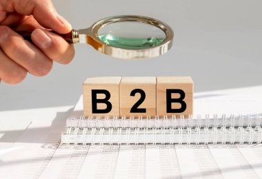 B2B kısaltması, ofis masasındaki tahta küpte işten işe, erkek elinde büyüteç.