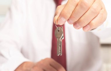 İş adamı emlakçı, ofis masasında oturan kırmızı kravatlı kameraya anahtar öneriyor..