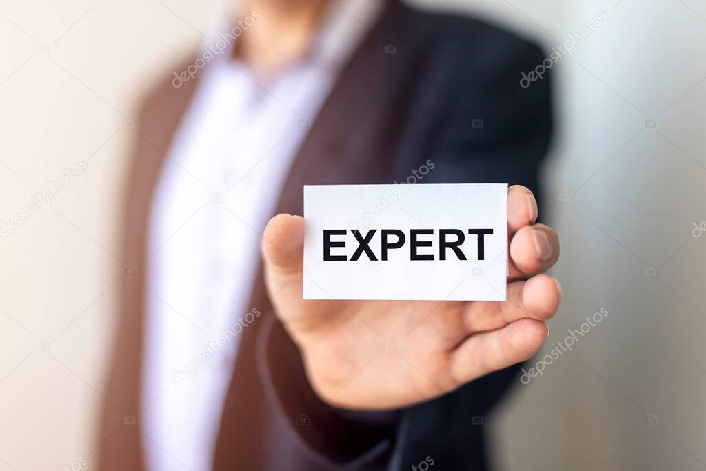 expert word written on paper board in hands of businessman over white wall