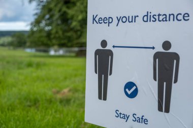 İngiltere 'de koronavirüs tecridi azalırken insanlardan sosyal olarak uzak durmalarını ve açık hava etkinliklerinde güvende olmalarını isteyen bir tabelanın yakın çekimi.