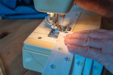 Kumaşı kontrol eden bir elin yakın çekimi ve dikiş makinesinin iğnesini birleştirerek insanların Coronavirus yüzünden takması gerektiği gibi ev yapımı bir maske yapmak.