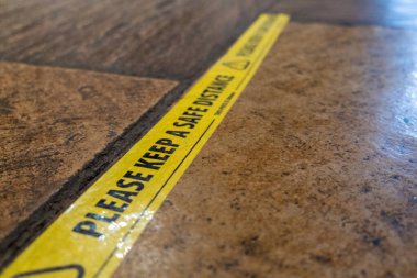Yellow tape on the floor of a pub to ensure that customers maintain social distancing clipart