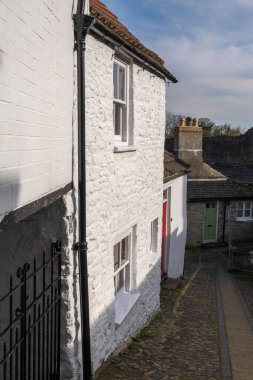 Richmond, Kuzey Yorkshire, İngiltere - 23 Mart 2020: Güneş ışığıyla aydınlatılan eski boyanmış beyaz tuğlalı binalarla dolu güzel bir kaldırım manzarası.