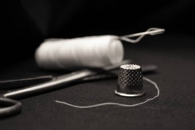 Dikiş makası, yüksük yakın plan, beyaz iplikler siyah arka plan, iğne zanaat