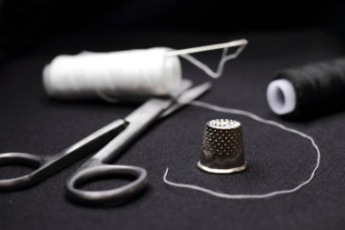 Dikiş makası, yüksük yakın plan, beyaz iplikler siyah arka plan, iğne zanaat