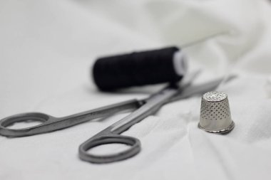 Beyaz zemin üzerinde iğne ve yüksük ile siyah iplik ve beyaz iplik makarası