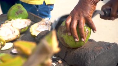 Bir sokak pazarında, bir adamın eline yaklaşıp büyük bir bıçakla inanılmaz bir şekilde hindistan cevizi kesiyor. Bir adam taze hindistan cevizi kesiyor. 