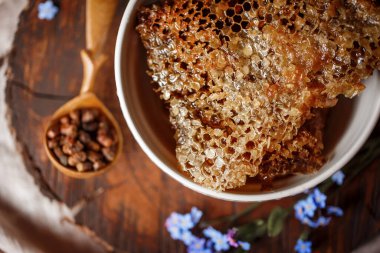 Taze taze bal, bal peteğinde beyaz bir kase üzerinde ahşap bir kahverengi kesim üzerinde keten bir masa örtüsü yanında keten kumaş, ahşap el yanında ahşap kaşık ve parşömen pergası ile parşömen ürünleri. 
