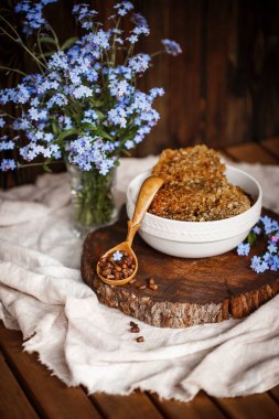 Ahşap kahverengi kaşık arı ürünleri ile Perga arı parşömeninin yanında bal ve ahşap bir kahverengi kesikle keten bir masa örtüsü üzerinde mavi çiçekler ve parşömenin üzerinde bir çiçek.