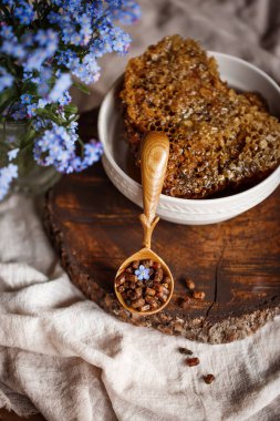 Ahşap kahverengi kaşık arı ürünleri ile Perga arı parşömeninin yanında bal ve ahşap bir kahverengi kesikle keten bir masa örtüsü üzerinde mavi çiçekler ve parşömenin üzerinde bir çiçek.