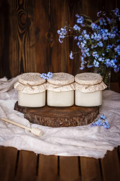 Tahta bir kahverengi üzerinde yan yana duran üç kavanoz çiğ organik bal ahşap bir masa örtüsü üzerinde ahşap bir masa örtüsü mavi çiçeklerin yanında ahşap kahverengi bir arka plan 