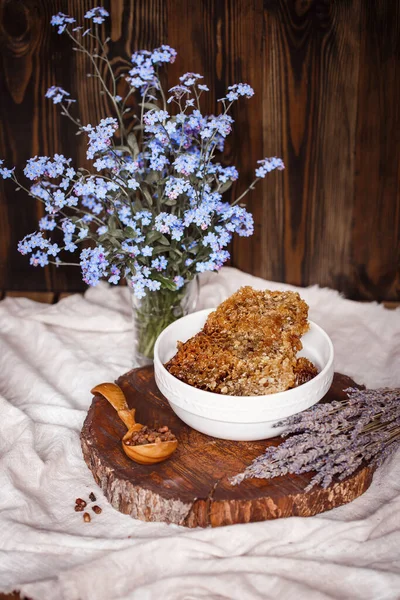 Çiğ organik bal, bal peteğinde beyaz bir plaka üzerinde ahşap kahverengi bir testerenin üzerinde keten bir masa örtüsü yanında lavanta, Perga ve arı ürünleri olan bir kaşık.