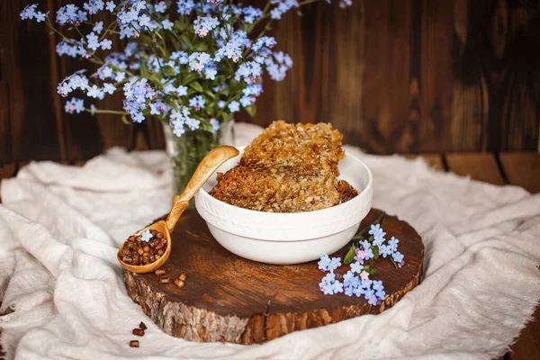 Ahşap kahverengi kaşık ve arı ürünleri ile Perga parşömeni yanında organik çiğ bal, ahşap kahverengi bir kesikle keten bir masa örtüsü üzerinde mavi çiçekler ve parşömenin üzerinde bir çiçek.