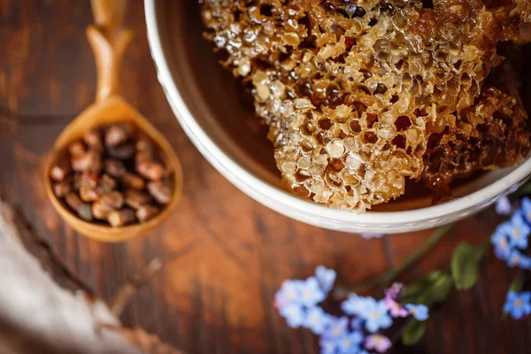 Taze taze bal, bal peteğinde beyaz bir kase üzerinde ahşap bir kahverengi kesim üzerinde keten bir masa örtüsü yanında keten kumaş, ahşap el yanında ahşap kaşık ve parşömen pergası ile parşömen ürünleri. 