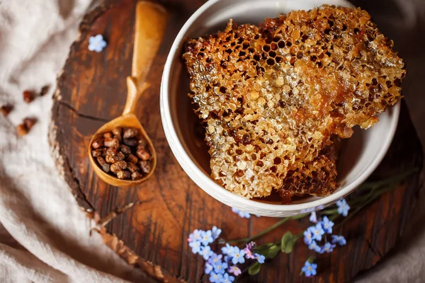 Taze taze bal, bal peteğinde beyaz bir kase üzerinde ahşap bir kahverengi kesim üzerinde keten bir masa örtüsü yanında keten kumaş, ahşap el yanında ahşap kaşık ve parşömen pergası ile parşömen ürünleri. 