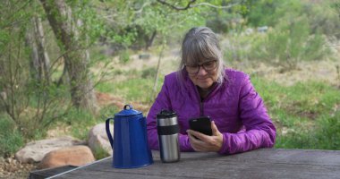 Açık havada doğanın içinde smartphone okuma bankta oturan yaşlı kadın uzun yürüyüşe çıkan kimse