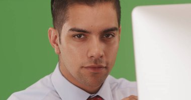 Yeşil ekranda kameraya bakarak bilgisayarda oturan Latin işadamı