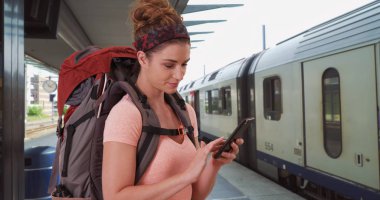 Tren istasyonunda Smartphone kullanarak sırt çantası takmış çekici genç bayan