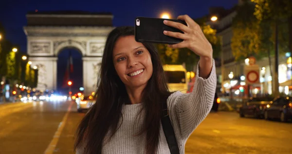 美丽的女性采取手机自拍在晚上与凯旋门为后 — 图库照片