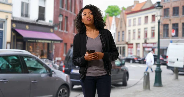 Pretty black woman walking through the city stopping to use her phone