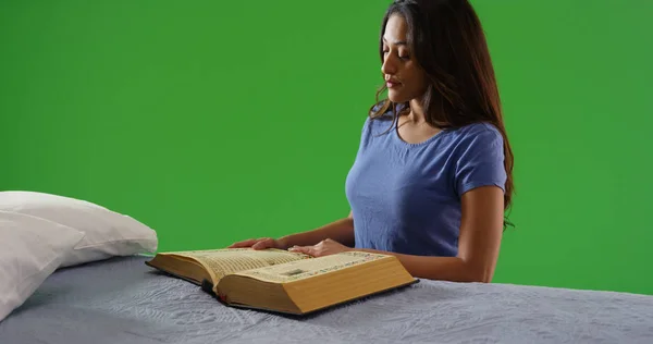 Faithful Latina reading religious text kneeling at bedside on green screen