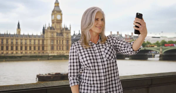 Older woman traveling in London takes a selfie on her smartphone