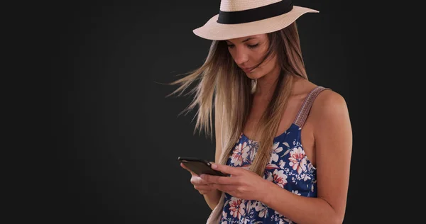 Millennial girl in romper and fedora texting on phone on gray background